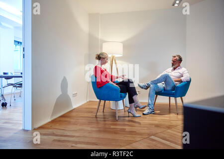 Reifer Mann und junge Frau sitzt im Sessel sprechen Stockfoto