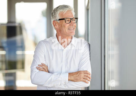 Unternehmer im Amt lehnte sich gegen Fenster, mit gekreuzten Armen Stockfoto