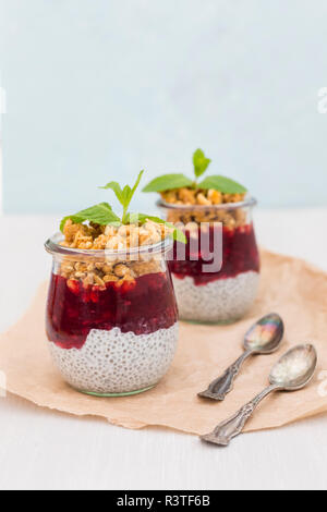 Zwei Gläser von Chia Pudding mit Kokosmilch, Rote Grütze und Erdnuss Müsli nachfüllen Stockfoto