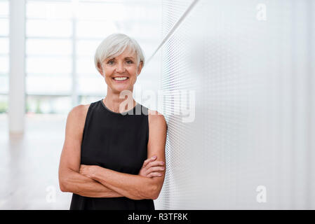 Portrait von lächelnden älteren Frau mit schwarzen Kleid gegen eine Wand gelehnt Stockfoto