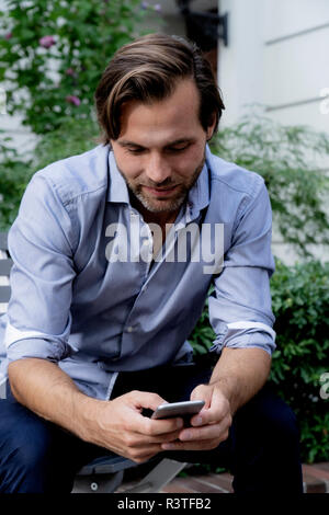 Mann sitzt auf Stuhl im Garten mit Handy Stockfoto