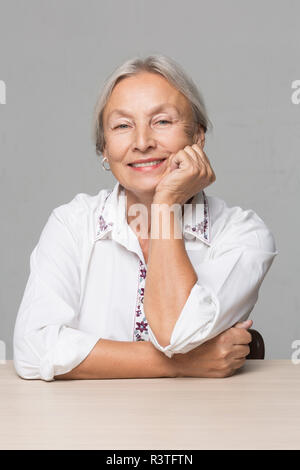Portrait der älteren Frau mit grauen Haaren sitzen am Tisch mit dem Kopf in der Hand. Stockfoto