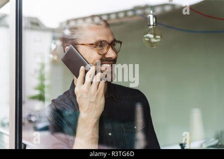 Lächelnden jungen Geschäftsmann auf Handy im Büro hinter Fensterglas Stockfoto