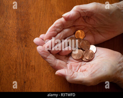 In der Nähe der Hände des älteren Frau pennies Holding. Von oben mit einem Holztisch im Hintergrund und kopieren Raum fotografiert. Stockfoto