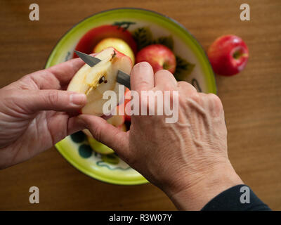 In der Nähe der Hände einer Frau coring Eine organische honeycrisp Apple mit dem Zinn Schale mit Äpfeln auf einem hölzernen Tisch im Hintergrund. Stockfoto