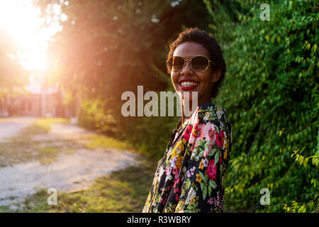 Porträt der glückliche junge Frau mit Sonnenbrille im Freien bei Sonnenuntergang Stockfoto