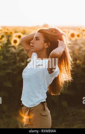 Portrait einer jungen Frau, die in einem Feld mit Sonnenblumen, Hände in Haar Stockfoto