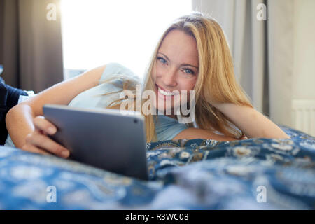 Lachende junge Frau auf dem Bett zu Hause liegen, mit digitalen Tablet Stockfoto