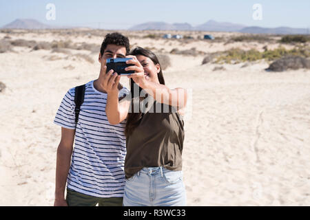 Ein junges Paar, das Spaß am Strand, wobei Smartphone selfies Stockfoto