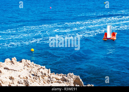 Bild der ruhigen Meer Oberfläche. Nahaufnahme einer orange Tretboot im tiefen blauen Wasser gegen schaumig auf dem Hintergrund verfolgen. Warmer Tag im Herbst. Konzept der Lei Stockfoto