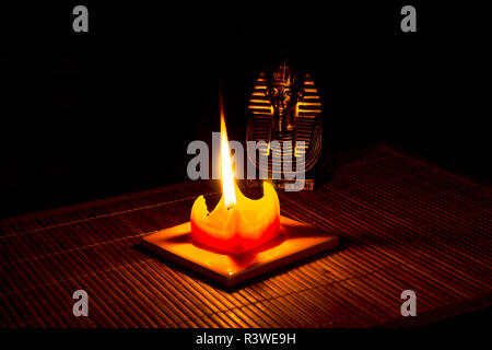 Statue des Tutanchamun beleuchtet durch eine Kerze auf Bambus Matte auf einem schwarzen Hintergrund. Stockfoto