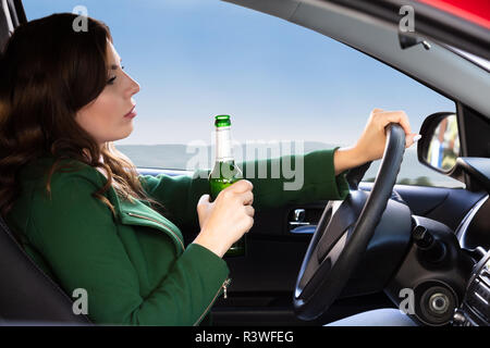 Seitliche Sicht auf eine schöne junge Frau mit Bier Flasche während der Fahrt Auto Stockfoto