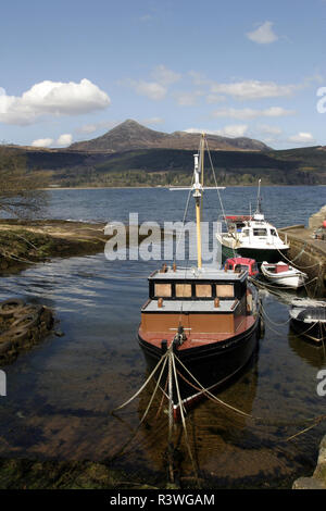 Ein paar kleine Fischerboote sind bis zu einem Steg in einer Bucht auf der Insel Arran gebunden, in den Firth of Clyde, Schottland. Goatfell, dem höchsten Punkt der Insel, können im Hintergrund gesehen werden. Arran, wird als, Cotland in Miniatur" bezeichnet, weil für eine breite Palette von atemberaubenden Landschaften. Stockfoto