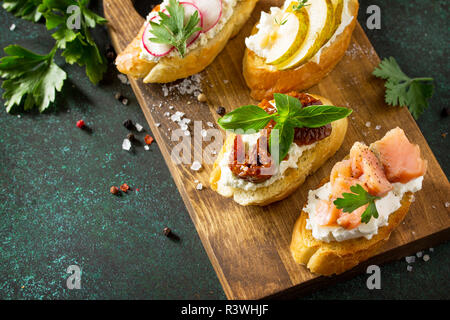 Italienische Antipasti Snacks für Wein. Vielzahl Brushetta mit Frischkäse, Birne, Rettich, Lachs und getrockneten Tomaten auf einem rustikalen Holzbrett serviert auf Stockfoto