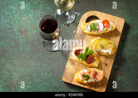 Italienische Antipasti Snacks für Wein. Vielzahl Brushetta mit Frischkäse, Birne, Rettich, Lachs und getrockneten Tomaten auf einem rustikalen Holzbrett serviert auf Stockfoto