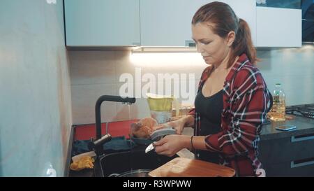 Mädchen beim Abwasch in der Küche Schneidebrett. Frau Köche in der Küche. Mädchen wäscht ein Messer auf in der Wanne unter dem Wasserhahn lifestyle Konzept Stockfoto