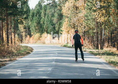 Training ein Athlet auf der Walze Skater. Biathlon Fahrt auf dem Roller Ski mit Skistöcke, im Helm. Herbst Training. Roller Sport. Erwachsene Mann rid Stockfoto
