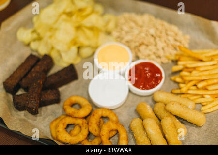 Lagerbier und Snacks auf Holztisch. Nüsse, Chips, Erdnüsse, Toast, Cracker. Vorspeise fast food. Handwerk Bier. Beerboard. Tomaten, Käse und Knoblauch sauc Stockfoto