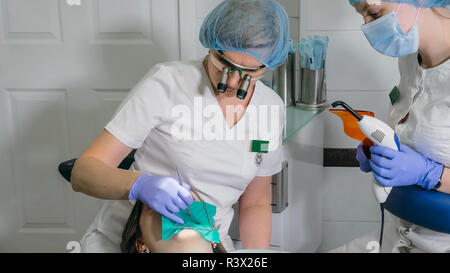 Frau beim Zahnarzt Klinik erhält der zahnmedizinischen Behandlung ein Loch in einen Zahn zu füllen. Zahnersatz und Verbundmaterial Polymerisation mit UV-Licht und Stockfoto