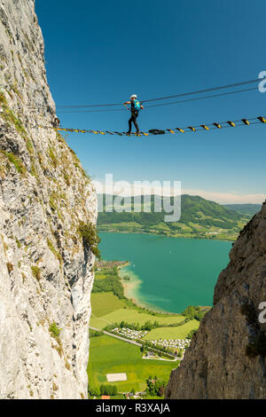 Bergsteiger zu Fuß auf einer hohen Brücke auf Drachenwand Klettersteig über den Mondsee, Österreich Stockfoto