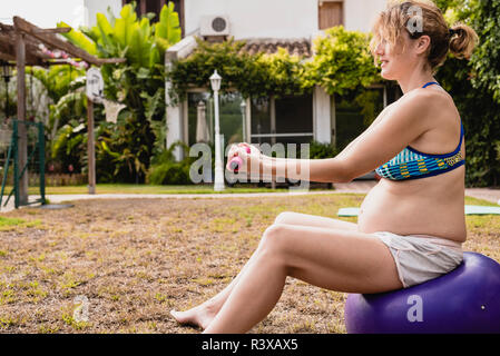 Schwangere Frau heben Gewichte auf Fitness Ball Stockfoto