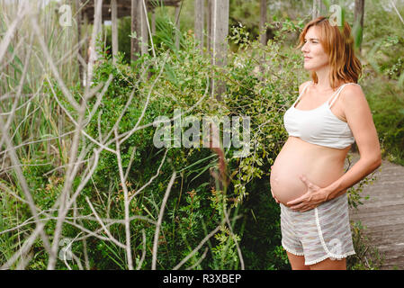 Schwangere Frau zu Fuß zwischen Bäumen und der Natur. Stockfoto