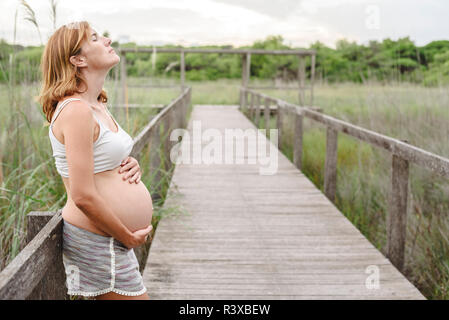 Schwangere Frau zu Fuß zwischen Bäumen und der Natur. Stockfoto