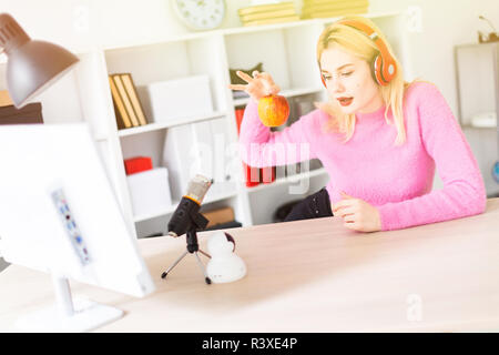 Ein junges Mädchen mit Kopfhörern am Tisch sitzen und mit einem Apfel. Stand vor ihr Mikrofon. Stockfoto