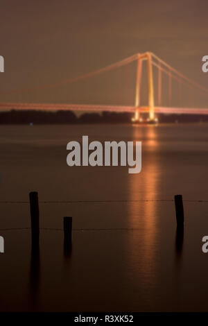 Ein Stacheldrahtzaun in das Wasser des Rheins führen. Die berühmte Hängebrücke von Emmerich im Hintergrund. Stockfoto