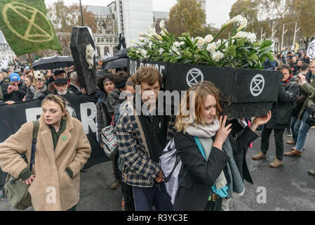 London, Großbritannien. 24. November 2018. In von ihren Sarg Aussterben Rebellion Mitkämpfern begraben verhindert worden, tragen es aus dem Parlament Square bis zu Linie eine Prozession hinter sich zu bilden, durch den Trommler und Trompeter geführt. Sie Langsam gingen, Whitehall und kurz sich auf die Straße, um in Stille sitzen stoppen, wenn der Sarg Downing St. erreicht, wenn die Prozession auf verschoben, andere Lagen in der Straße das Aussterben Rebellion Symbol für einige Minuten, bevor der Rest auf dem Weg nach unten die Mall zum Buckingham Palace. Stockfoto