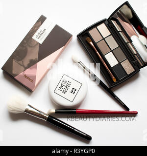 Flatlay der Make-up-Pinsel mit grauen Eyeshadowpalette, Make up Pinsel und Kissen Stiftung auf weißem Hintergrund Stockfoto