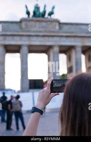 Hände halten Telefon Handy und nimmt Bilder der berühmten historischen Sehenswürdigkeiten. Das Brandenburger Tor neoklassizistisches Denkmal in Berlin. Stockfoto