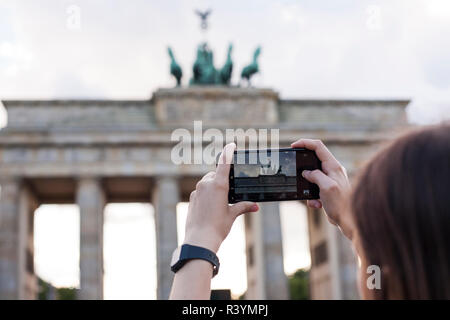 Hände halten Telefon Handy und nimmt Bilder der berühmten historischen Sehenswürdigkeiten. Das Brandenburger Tor neoklassizistisches Denkmal in Berlin. Stockfoto