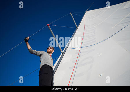 Schöne und selbstbewusste junge Mann steht auf Yachtcharter board und im Meer durch die Brille schauen. Er liegt am Rande der Yacht. Guy Holding segeln Seil in der Hand. Junge Mann ist glücklich und friedlich. Stockfoto