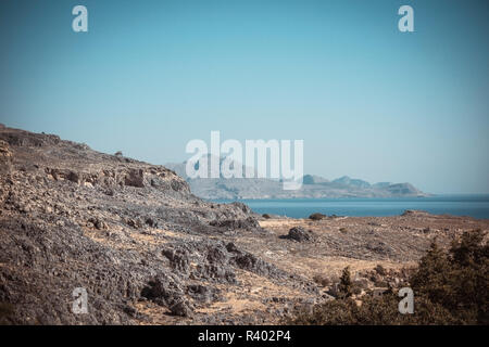 Horizontale Foto mit Trockene Felsen nur von Steinen bedeckt. Die Felsen sind braun und grau. Die Felsen sind neben der berühmten Stadt Lindos auf Rhodos. Himmel und Meer ein Stockfoto