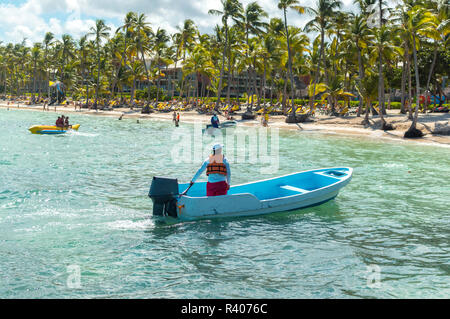 Das Bereitschaftsboot und die Menschen entspannen am Strand unter Palmen im Ferienort Punta Cana. Stockfoto