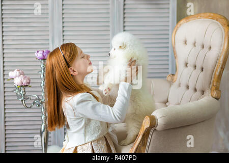 Portrait von Ingwer Haare Mädchen spielen mit Husky poppy. Modell Mädchen mit roten Haaren posiert im Studio Shooting mit Sammy weiße Welpen beim Sitzen auf Royal Retro Stockfoto