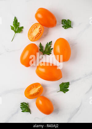Orange Tomaten auf weißem Marmortisch. Gelb oder Orange Tomaten mit zwei halben aufgeschnittenen Tomaten und frischer Petersilie. Top View oder flach. Vertikale Komposition. Stockfoto