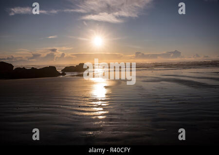 Cannon Beach, Oregon. Sunburst, wie die Sonne über dem pazifischen Ozean, Tide Pools, haystack Rocks, und nasser Sand Stockfoto