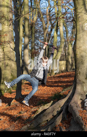 Pre Teen Boy Schwingen am Seil in den Wäldern im Herbst Stockfoto