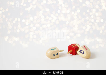 Happy Chanukka Grußkarte, Einladung der traditionellen jüdischen Lichterfest Urlaub Symbole. Holz- Dreidel Spielzeug auf weißer Tisch. Festlich glitzernden goldenen bokeh Lichter Hintergrund. Der leere Raum. Stockfoto