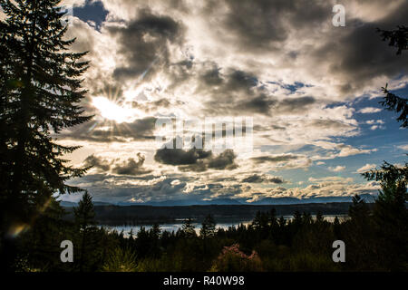 Bremerton, Washington State. Sunburst bricht durch Silber Wolken und blaue Flecken Himmel über dem Puget Sound und grünen Wald Stockfoto