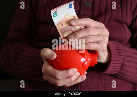 Rentner setzt Geld in das Sparschwein. Stockfoto