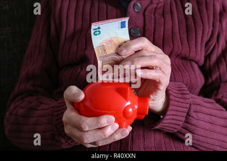 Rentner setzt Geld in das Sparschwein. Stockfoto