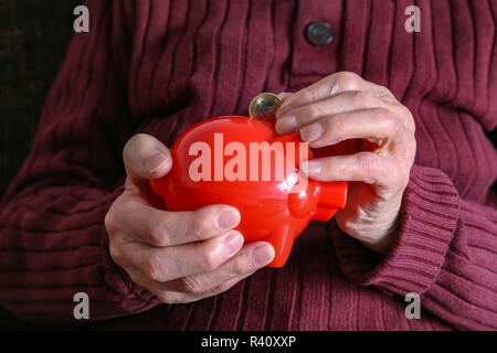 Rentner setzt Geld in das Sparschwein. Stockfoto