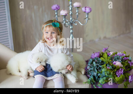 Portrait von blond Baby Mädchen spielen mit Husky Welpen. Modell Mädchen mit blondem Haar posiert im Studio Shooting mit Sammy weiße Welpen während auf Royal retr-Sitzung Stockfoto