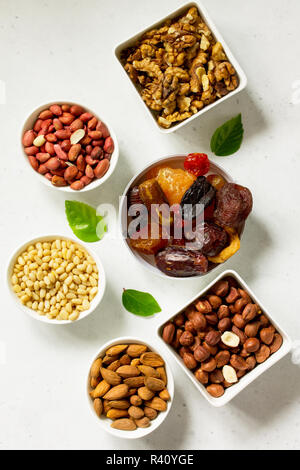 Verschiedene Nüsse in einer Schüssel aus Keramik und getrocknete Früchte auf einem Tisch aus Stein. Das Konzept einer gesunden Nachtisch. Ansicht von oben flach Hintergrund. Stockfoto