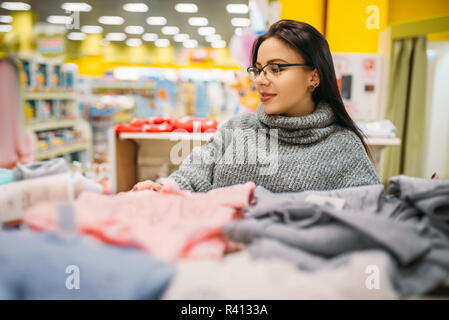 Fröhliche Zukunft Mutter in Gläser kauft Kleidung der Kinder im Store für Neugeborene. Schwangere Frau im Shop von Waren für Kleinkinder Stockfoto