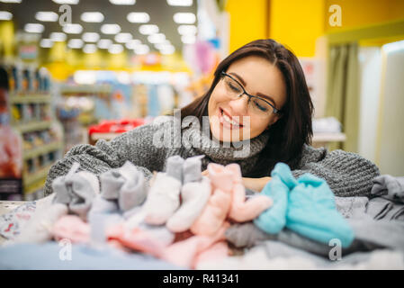 Fröhliche Zukunft Mutter in Gläser kauft Baby Kleidung im Store für Neugeborene. Schwangere Frau im Shop von Waren für Kleinkinder Stockfoto