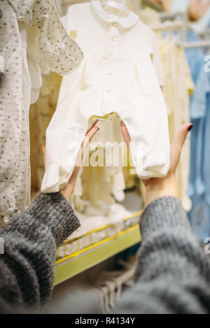 Weibliche Person wählt Baby Kleidung im Store für Neugeborene. Schwangere Frau im Shop von Waren für Kleinkinder Stockfoto